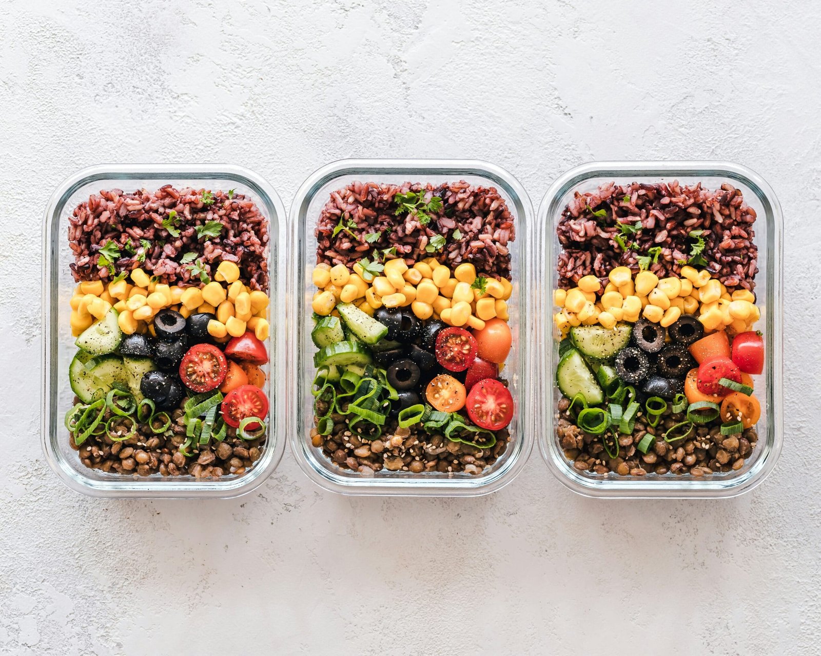 Colorful vegetarian meal prep ideas with bowls of rice and salad vegetables in glass containers